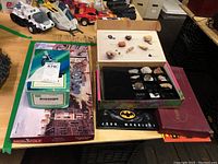 Photo of various items on a table including fossil kit open with fossils displayed, Sears microscope box, Batman book, Boston Monopoly board game partially visible, and Scrabble game box.