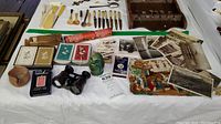 Wide view of lot showing postcards, playing cards, black binoculars, carved owl, and other vintage items on white tablecloth