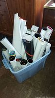 A blue plastic tub filled with over two dozen rolled posters stored upright.