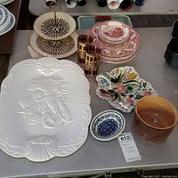 Front overview of the lot showing large white Roseville ceramic planter, Polish ceramic floral soap dish, red Johnson Bros transferware plates and bowls, gold-accented vintage cocktail glasses, and small Blue Ridge nut dish