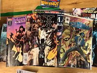 Top view showing various comic books including X Files 1998, Shadowman, and others overlapping on table.