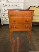 Front view of wooden nightstand with two drawers and wooden knobs, showing wear and scratches.
