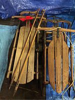 Three vintage sleds tightly grouped together alongside a pair of vintage ski poles, showing overall condition and size comparison.