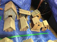 All seven vintage handcrafted wooden birdhouses displayed on blue tarp, showing varied sizes and designs, some with pitched roofs and circular openings.