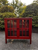 Front view of the red display cabinet showing glass paneled double doors and black knob handles.