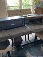 Two printers on a table showing Canon Pixma on left and HP Deskjet 3050A on right, illustrating condition and size.
