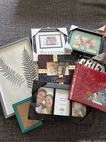 Photo shows 7 assorted photo frames and one red photo album arranged on a carpeted floor, displaying a variety of styles and some featuring sample photos.