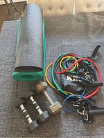 Overview of two 5 lb dumbbells, 10 lb dumbbell, yoga mats, and Kinzi stretch band set on grey surface