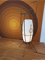 Full view of the vintage atomic lamp placed on a wooden surface with a circular pattern artwork in the background.