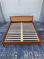 Full front view of teak bed frame with slatted base and woven headboard
