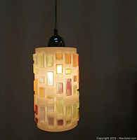 Pendant lamp lit, showing its drum-shaped glass shade with multicolored rectangular fused glass decorations and chrome cap.