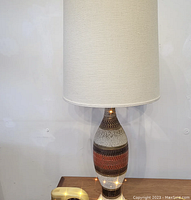 Full view of the vintage table lamp showing the tall fabric shade and ceramic base on a wooden surface.