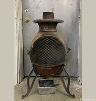 Full front view of the rusted vintage cast iron firepit showing mesh door, legs, and ash catcher below.