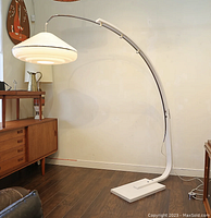 Full view of lamp in room showing curved white metal frame and base with hanging pendant shade