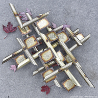 Overall view of the vintage mid-century modern metal wall art sculpture on concrete with some fallen leaves.