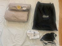 Folded queen size Coleman Quickbed air mattress with visible yellow built-in pump valve alongside black storage bag and instruction manual.