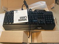 Front view of the HAVIT Magic Eagle gaming keyboard out of the box with user manual and wired USB cable visible.