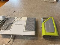 Photo showing two speakers: InMotion Altec Lansing speaker in white and gray with power cord, and the Lifeproof Aquaphonics AQ9 speaker in lime green and gray with handle