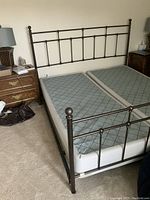 Photo showing the fully assembled king size bed frame with headboard, footboard, side rails, and box spring with two mattresses on carpet.
