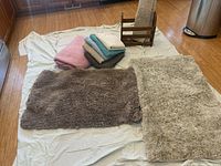 Two plush area rugs and pile of folded towels and fleece blanket on floor
