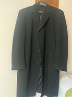 Full view of black men's dress coat hanging showing length and front buttons.