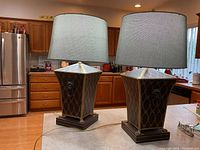 Pair of brown metal base lamps with gold/bronze diamond pattern and lion head sides, topped with blue cloth drum shades on kitchen counter.