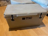 RTIC cooler closed, displaying tan exterior with black latches and RTIC branding on lid and front.