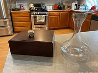 Photo showing the wooden humidor box closed next to the clear glass wine decanter, displayed on kitchen counter.
