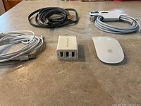 Apple Magic Mouse, charging cords, USB wall charger, and Ethernet cables arranged on a table