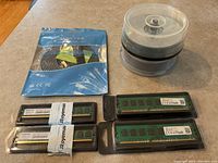 Two sealed 2GB DDR2 RAM modules, two sealed 8GB DDR3 RAM modules, a sealed Cat7 Ethernet cable in blue packaging, and a spindle of blank discs.