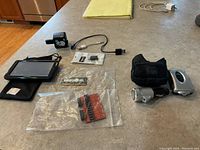 Image showing all items of the lot placed on a table: Garmin GPS with black case, iGo charging kit, power adapter, microchip modules in clear plastic bag, 4GB DDR4 RAM.