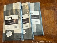 Photo of three sealed packs of No. 918 curtain tiers, showing gray buffalo plaid fabric pattern and packaging labels.