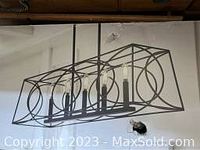 Photo of the assembled pendant light showing black metal frame with circular side decorations and five candle-style lights.