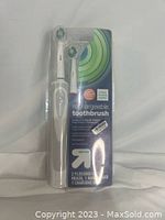 Photo of the up&up rechargeable toothbrush sealed in plastic packaging showing the handle and one attached brush head, along with the charging base and extra brush head behind packaging.