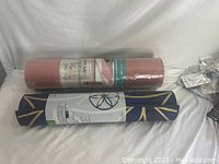 Both yoga mats together showing the Gaiam reversible mat with printed design and the 8mm TPE mat rolled and sealed in plastic.