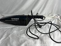 Side view of the black Singer handheld vacuum with power cord laid out showing brand and model details.