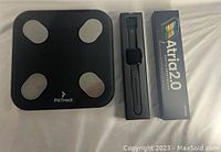 FitTrack smart scale alongside Atria 2.0 smartwatch in box and packaging, showing both items included in the bundle