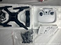 HJHRC black quadcopter drone with propellers, white remote controller, instruction manual, and small parts in plastic bag seen in protective foam packaging.