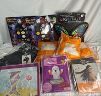 Photo showing 4 packs of white spider web decorations, 1 ring toss game, 1 pair of light-up butterfly wings, 2 makeup sets, a black cape, a wig, and the packaged mermaid tail costume accessory with headband.