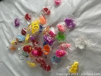 Photo showing a large assortment of approximately 42 small squishy and mochi toys scattered loosely, each individually wrapped in clear plastic, with multiple colors and shapes visible.