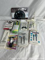 Tech accessories arranged on white fabric including multiple cables, adapters, VGA cable, smart stand, and mini microphone, all new in packaging.