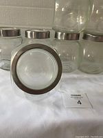 Set of eight glass holding containers with silver metal lids, clear rounded square shaped containers.