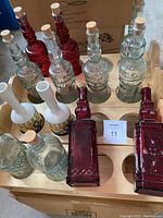 Top-down view of multiple empty decorative glass bottles in clear and red glass, all topped with cork stoppers, placed inside wooden holders designed for bottle storage.