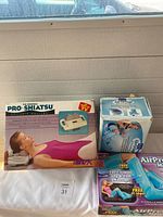 Photo showing three boxed massagers on white cloth, including Pro-Shiatsu and two AirPress models for legs and feet.