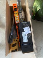 Box with orange level, black toolbox, handsaw and pipe wrench