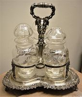 Front view of the silver-plated Art Nouveau style holder with three glass bottles labeled Gin and Scotch visible, ornate handle and floral/acorn decoration