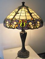 Full view of large stained glass lamp illuminated showing the stained glass shade's floral design with warm light and the ornate dark metal base.
