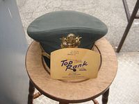 Front view of smaller cap on wooden stool with gold eagle insignia and Top Rank Louisville manufacturer card.