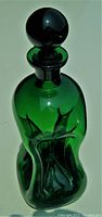Front angled view of emerald green glass decanter with ball stopper on a white background, showing the sculptural glug-glug body shape.