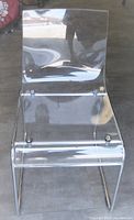 Front view of transparent Lucite chair showing clear seat and backrest fixed with visible chrome screws on chrome frame.